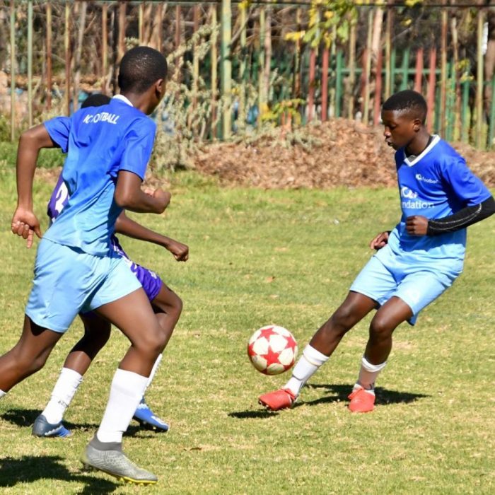Image of 3 young teenagers playing football in blue soccer outfits with a white ball with red stars printed on it