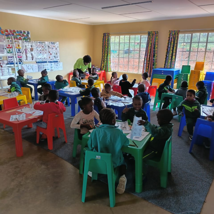 Image of orphaned pre-school learners in a classroom with their teacher, working with pencils and pictures at a Kenosis Early Childhood Development Centre