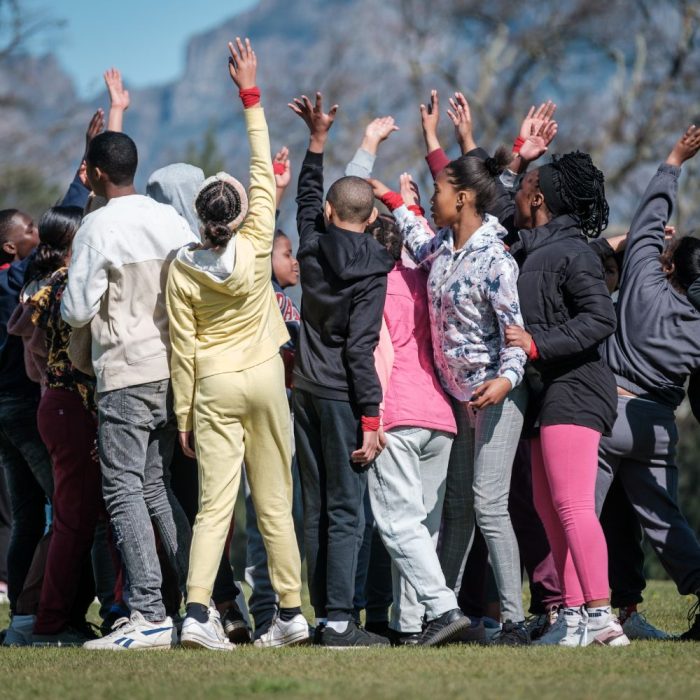 Image of primary school learners with their hands in the air at an experiential learning camp at Bridges Retreat Centre in Franschhoek, providing a life-impacting outdoor education experience - a mountain in the background