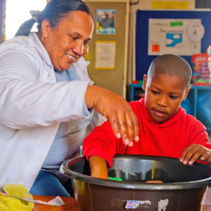 Image of an intellectual disabilities teacher teaching a boy through play with their hands in a container with objects and water