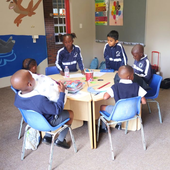 Image of 6 neurodiverse primary school learners sitting around a square table busy with crafts